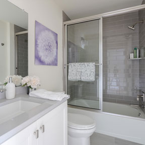 Bathroom with glass shower and tub combination, toilet, and vanity with cabinets for storage