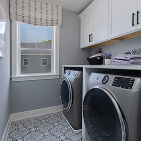 Laundry room of the Hamilton model with window, tile floor, washer and dryer, and cabinets