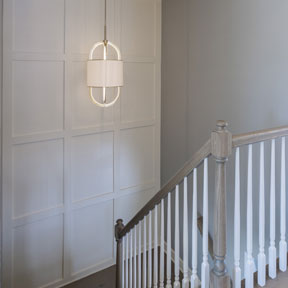 Medium tone wooden staircase featuring decorative wall paneling at the Hamilton model home in Chalfont, PA