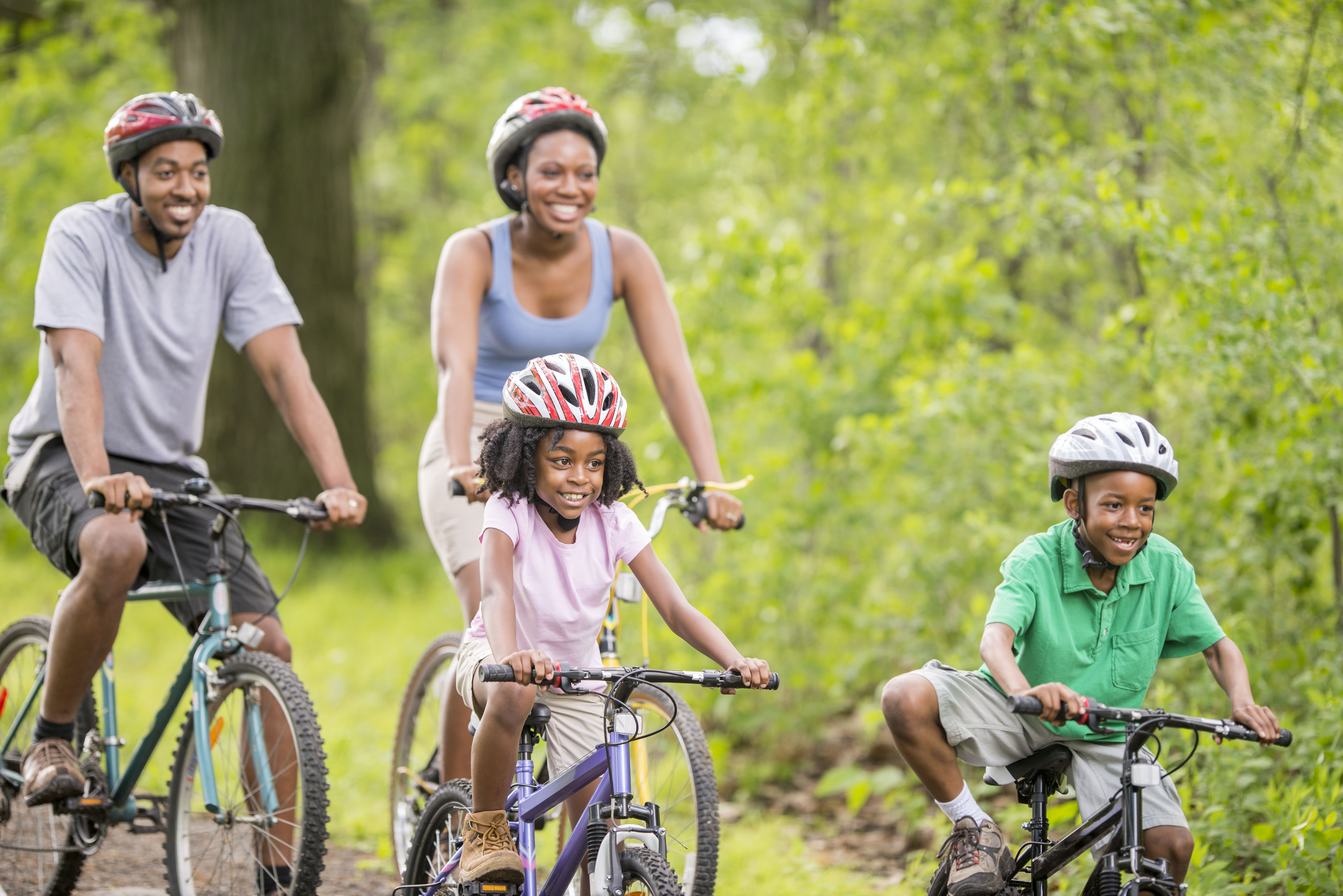 A family is going on a bike ride through the woods while on summer vacation.