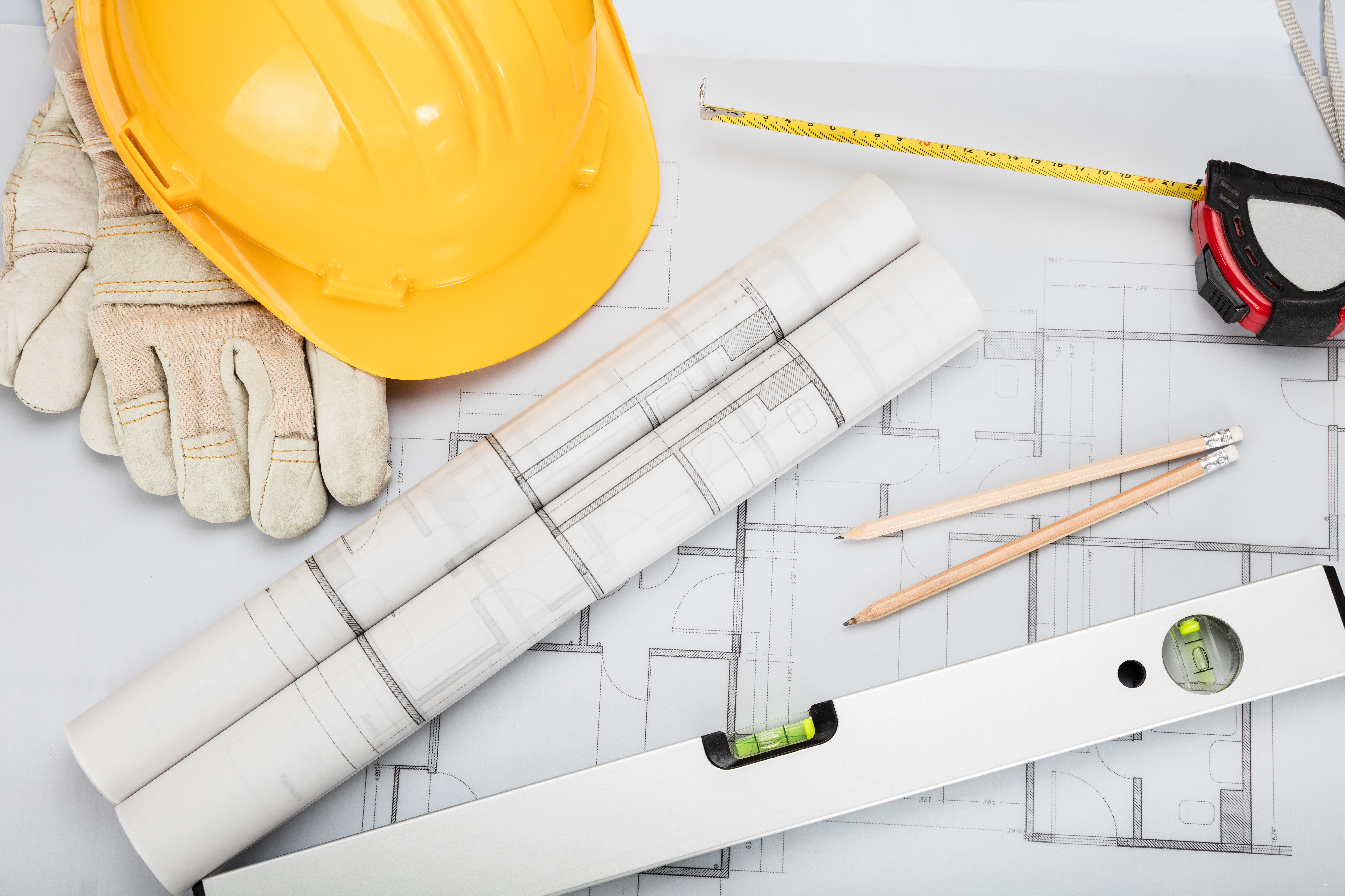 Construction hat and gloves on top of floor plan blue print designs